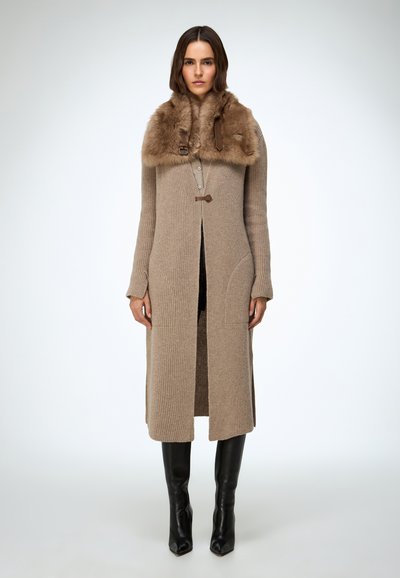 Beżowy długi kardigan z prążkowanego dzianiny z futrzanym kołnierzem, skórzanymi akcentami i przednim rozcięciem. Skomponowany z czarnymi kozakami sięgającymi do uda.