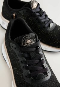 Scarpe da ginnastica nere con superiore in maglia testurizzata, caratterizzate da spruzzi metallici dorati, design con lacci neri e dettagli bianchi nella suola.