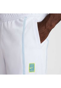 Hvite sportsshortser med lyseblå sømmer, med en lomme og et grønt og blått Nike-logo på låret.