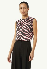 Ärmelloses Oberteil aus seidigem Stoff mit einem schwarz-pinken Zebra-Muster, mit plissiertem Ausschnitt, kombiniert mit hochgeschnittenen schwarzen Hosen.