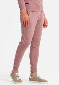 Helle rosa Sweatpants aus weichem Material mit gerippten Bündchen, seitlichen Taschen und einem schmalen Schnitt, kombiniert mit beigen Sneakers.