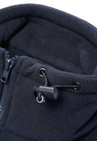 Gros plan sur le col d'une veste polaire bleu marine avec fermeture éclair et cordon de serrage ajustable avec un verrou en plastique.