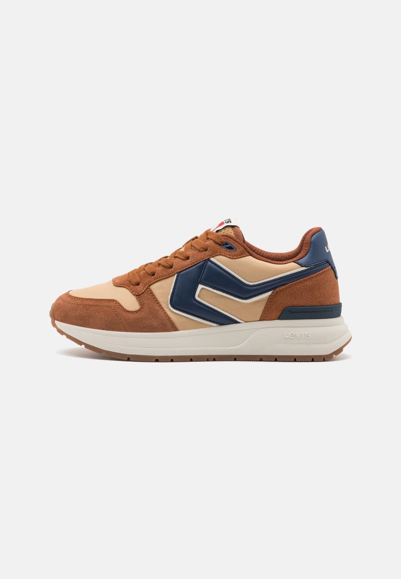 Vue latérale d'une basket marron et beige avec des accents bleu marine et une semelle blanche sur un fond clair uni.