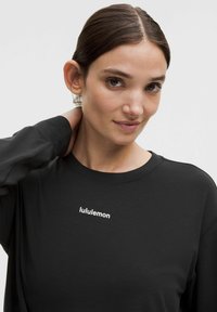 Čierna blúzka s dlhým rukávom vyrobená z mäkkej tkaniny, s okrúhlym výstrihom a bielym logom "lululemon" na hrudi.