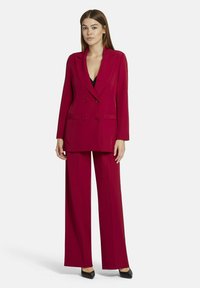 Rode dubbelzijdige blazer met geknipte revers en twee voorkeizen, gecombineerd met wijde broek in bijpassende kleur. Soepele stofstructuur.