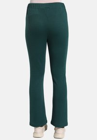 Green ribbed knit pants with a relaxed fit, featuring an elastic waistband and flared legs, paired with light-colored footwear.