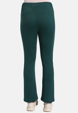 Pantaloni a coste verdi in maglia con una vestibilità comoda, dotati di un elastico in vita e gambe svasate, abbinati a calzature di colore chiaro.