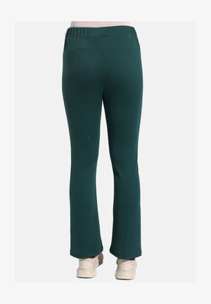 Vihreät ribattuja neulehousuja rentoa leikkausta, joissa on joustava vyötärö ja levenevät lahkeet, yhdistettynä vaaleisiin jalkineisiin.