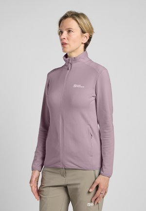 Hellblaues Zip-up-Jackett aus strukturiertem Material mit Seitentaschen und einem Logo auf der Brust, kombiniert mit beigen Hosen.