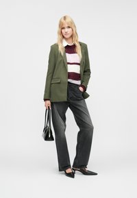 Zelený blazer na pruhovanom bordovom, bielom a ružovom svetri, skombinovaný s čiernymi džínsami a čiernymi topánkami s nízkym opätkom. Drží čiernu kabelku.