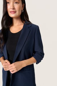 Navy blue blazer with a smooth texture, single-button front, and rolled sleeves. Paired with a black ribbed top underneath.