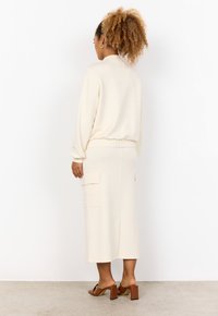 Set di loungewear color crema composto da un top dal taglio rilassato e una gonna midi con tasche a toppa. La gonna presenta una sottile texture e una vita elasticizzata.