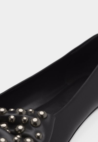Μαύρο επίπεδο παπούτσι με στρογγυλεμένη μύτη, διακοσμημένο με συγκεντρωμένες γυαλιστερές μεταλλικές τρουκς στο μπροστινό πάνω μέρος.