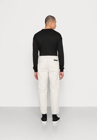 Maglietta nera a maniche lunghe abbinata a pantaloni bianchi con vita elastica e tasca posteriore. Sneakers nere completano l'outfit.