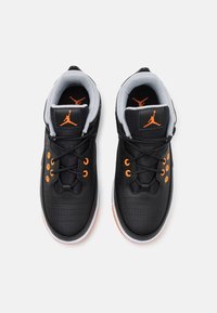 Zapatillas negras con acentos naranjas, que presentan un diseño de cuero perforado, cuello acolchado y suelas de goma. Incluyen cierre con cordones y el logo de Jumpman.