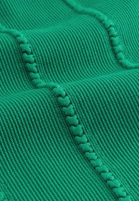 Zelená texturovaná látka s žebrovanými liniemi a vlnitým vzorem s pevnými lemovacími prvky. Měkký materiál s plyšovým, příjemným povrchem.