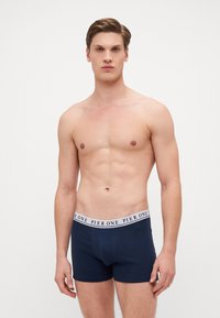 Tengerészkék pamut boxer nadrág fehér márkázott elasztikus derékszallaggal. A nadrág szoros illeszkedésű és sima tapintású.