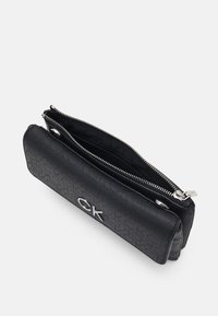 Portafoglio nero Calvin Klein con motivo a logo in rilievo, logo "ck" argentato, scomparto principale con zip e tasca frontale con chiusura a scatto su sfondo bianco.