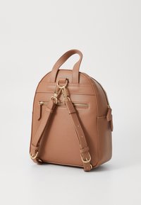 Béžový batoh z umělé kůže s kulatým tvarem, zlatými kovovými doplňky, horním madlem a nastavitelnými popruhy. Obsahuje přední kapsu na zip a texturovaný povrch.