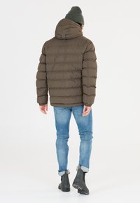 Brun puffjacka med huva, kviltad textur och elastiska manschetter, parat med ljusblå jeans och svarta ankelboots.