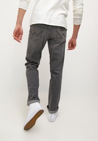 Grå denimjeans med slim fit, med två bakfickor och ett subtilt urtvistat mönster. Bärs med vita sneakers och en ljus skjorta.