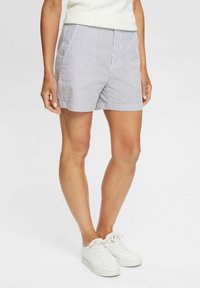 Shorts rayés bleu clair et blanc, en coton, coupe décontractée, poches latérales et taille élastique. Associés à des baskets blanches.