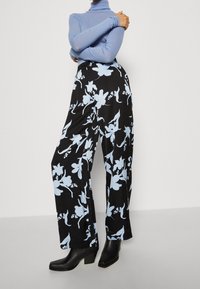 Czarne spodnie o szerokich nogawkach z dużym jasnoniebieskim kwiatowym wzorem, zestawione z dopasowanym jasnoniebieskim golfem i czarnymi botkami na klockowym obcasie.