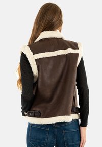 Chaleco de cuero marrón con borde de piel de oveja blanca, diseño sin mangas y correas ajustables con hebilla en la cintura. Textura suave y estilo clásico.