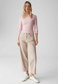 Hellrosa enganliegendes Langarmshirt mit rundem Ausschnitt, kombiniert mit beigen weit geschnittenen Hosen und weißen Sneakern. Einfaches, lässiges Design.