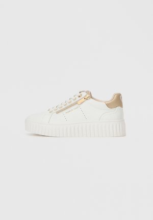 Valkoinen sneaker, jossa on uritettu pohja, kultaiset yksityiskohdat ja sivuvetoketju. Pinta on sileää nahkaa, jossa on ompeluseikkoja. Vahvistettu kantapää.