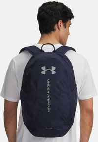 Zaino blu navy realizzato in tessuto resistente, dotato di un logo in rilievo, scomparti multipli e tasche laterali in rete per una maggiore capacità di stoccaggio.