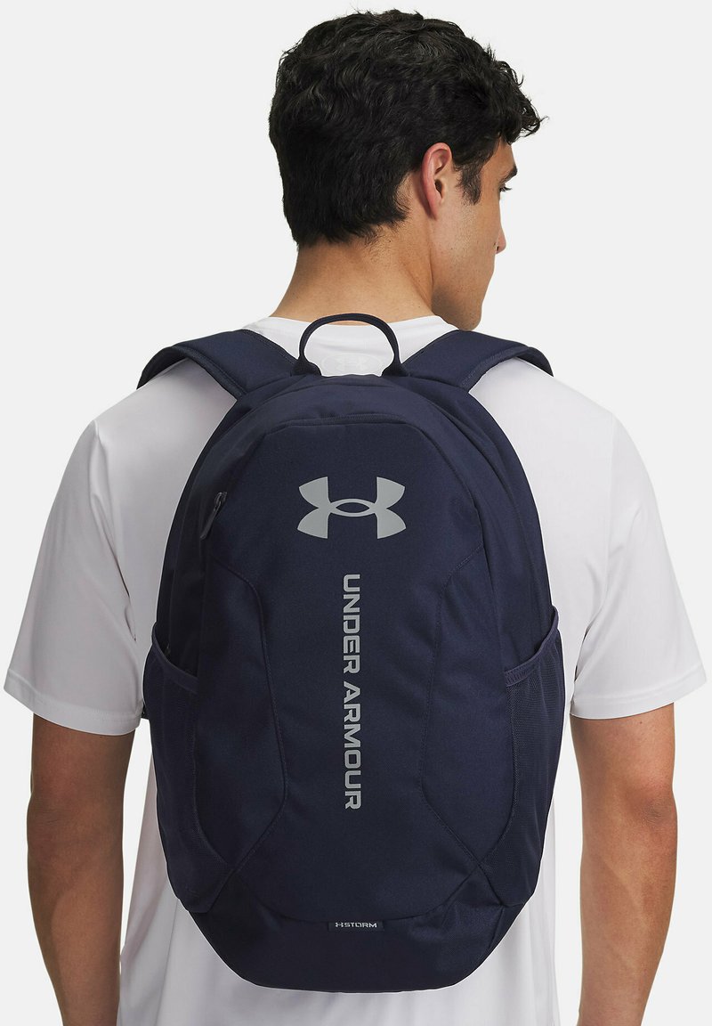 Zaino blu navy realizzato in tessuto resistente, dotato di un logo in rilievo, scomparti multipli e tasche laterali in rete per una maggiore capacità di stoccaggio.