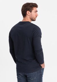 Marineblaues Langarm-T-Shirt aus Baumwolle, mit Rundhalsausschnitt, weicher Haptik und slim-fit Passform, kombiniert mit lässigen Jeans.