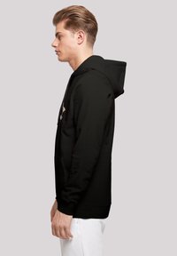 Svart hettegenser laget av mykt stoff, med kengurulomme, justerbar snorhette og ribbede mansjetter. Minimalistisk design uten mønstre.