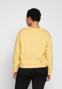 Sudadera amarilla con cuello redondo y mangas largas, con un ajuste relajado y puños de canalé. Fabricada con un tejido suave, combinada con jeans negros.