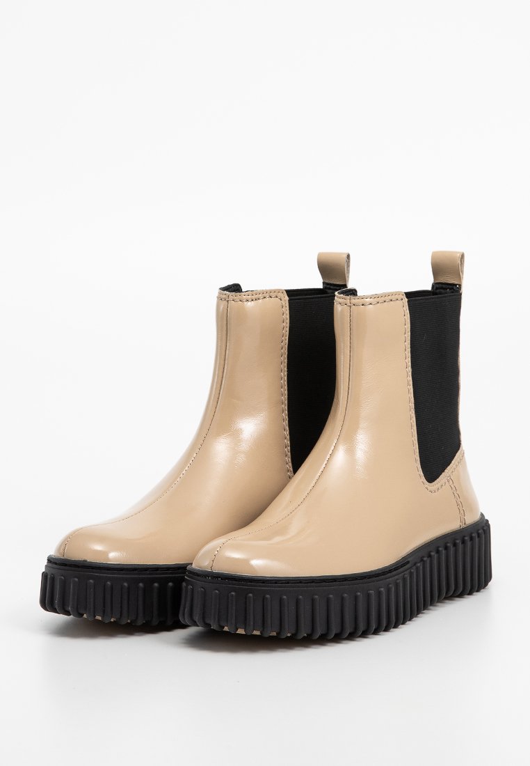 Stivaletti alla caviglia in pelle verniciata beige con pannelli elastici laterali neri, punte arrotondate e suole in gomma nera spessa con scanalature verticali.