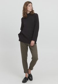 Top negru cu mâneci lungi, guler înalt și buzunar frontal, asortat cu pantaloni maro cu model houndstooth. Mocasini negri completează ținuta.