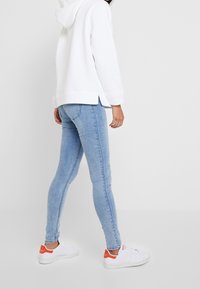 Biała, luźno dopasowana bluza z kapturem, zestawiona z jasnoniebieskimi skinny jeansami. Buty są białe z pomarańczowymi akcentami. Czysty, casualowy wygląd.