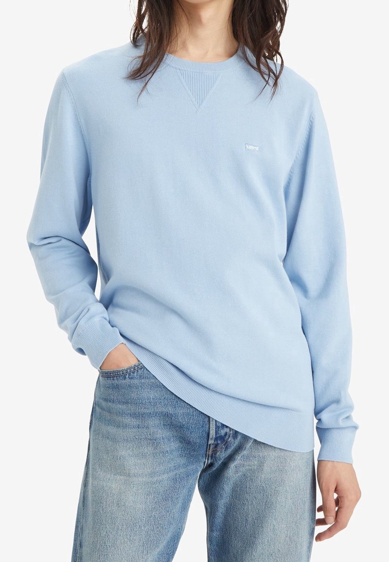 Ljusblå sweatshirt med rund halsringning tillverkad av mjukt tyg, med ribbade detaljer vid halsringningen och ärmarna, i kombination med blekta blå jeans.