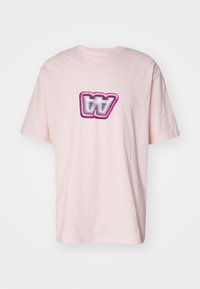 Camiseta de algodón rosa con un logotipo gráfico distorsionado en blanco y negro con un contorno rosa en el frente. Mangas cortas y corte relajado.
