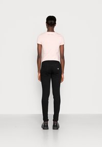 Sorte skinny jeans med høy midje, kombinert med en lys rosa T-skjorte med teksten "EST. 1981" i diskret skrift på ryggen. Glatt tekstur.