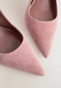 Tacones de aguja de ante rosa con punta afilada, forro interior suave y una textura sutil. Sin herrajes o acentos visibles.