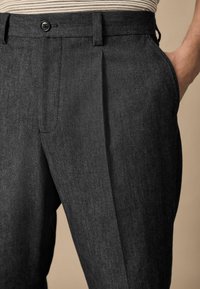 Pantalones ajustados de color gris oscuro, confeccionados con una tela texturizada, que presentan pinzas y un cierre de botón, con bolsillos laterales y un diseño entallado.