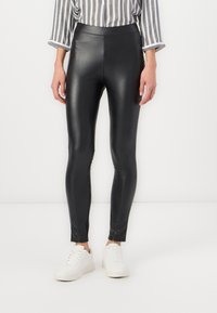Zwarte nepleer leggings met een gladde textuur, voorzien van een hoge tailleband en een slim fit, gecombineerd met witte sneakers en een gestreept shirt.