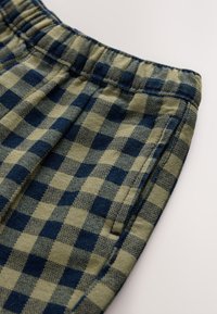 Kratke hlače z karo vzorcem v olivno zeleni in mornarsko modri barvi, z elastičnim pasom in žepi ob stranskih šivih. Mehka tekstura, priložnostna zasnova.