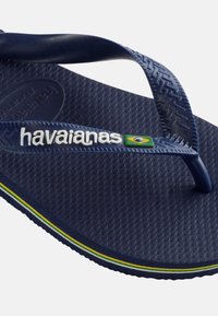 Tumesinised Havaianase plätud reljeefse tallaga, valge brändinimega rihmal ja väikese Brasiilia lipu detailiga varbavahel.