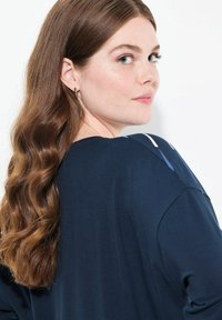 Marinblå långärmad topp med en avslappnad passform, som har kontrasterande vita och ljusblå accenter på axlarna. Mjuk tygkänsla.