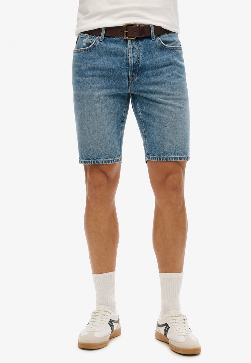 Shorts de mezclilla en azul claro con un diseño clásico de cinco bolsillos, dobladillo deshilachado y combinados con un cinturón marrón y zapatillas blancas.