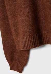 Brązowy sweter z miękkiej, teksturowanej tkaniny, z prążkowanymi mankietami i dołem. Zbliżenie podkreśla wzór dzianiny i bogaty kolor.
