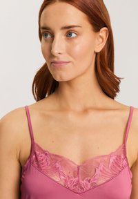 Lyserød kamisol med blonder detaljer ved halsudskæringen; tynde stropper, glat stof, med indviklede blomsterblonde mønstre og en tætsiddende pasform.